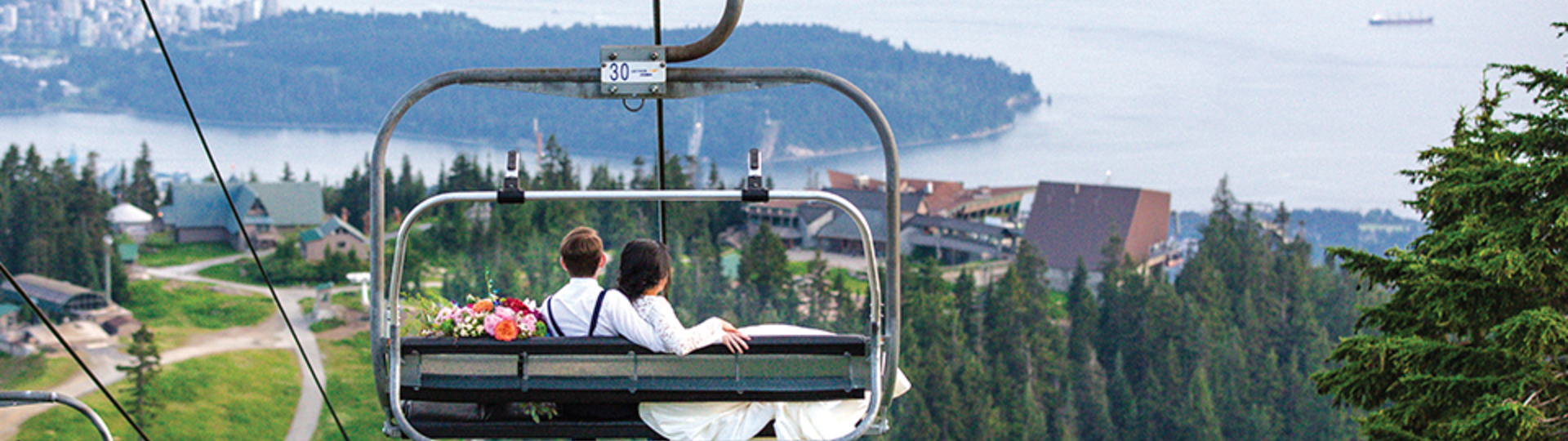 wedding day couple riding chairlift down to Chalet with view of Vancouver in background